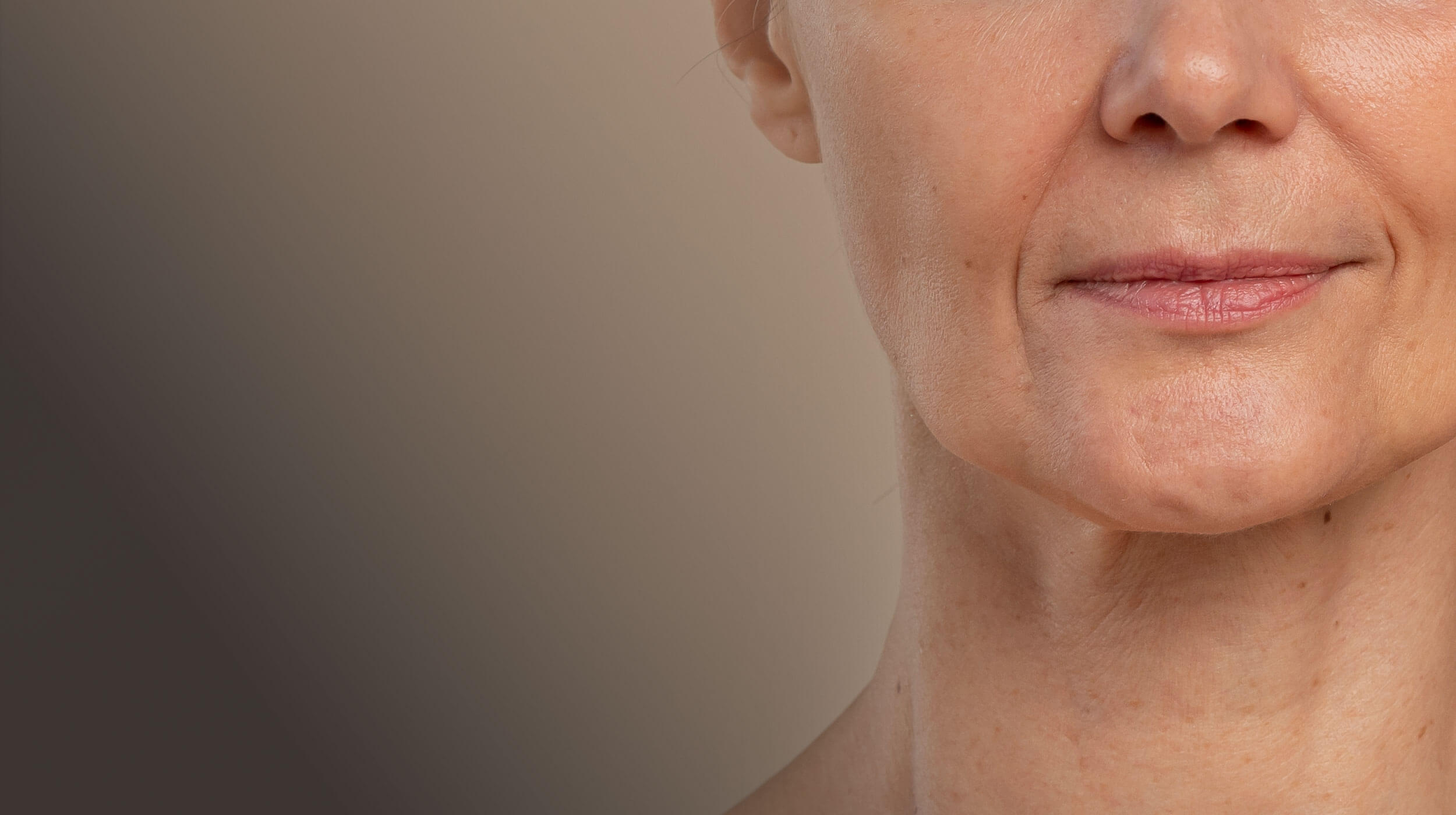 Κοντινό πλάνο του λαιμού και του προσώπου μιας γυναίκας, με εμφανείς λεπτές ρυτίδες και απώλεια ελαστικότητας.