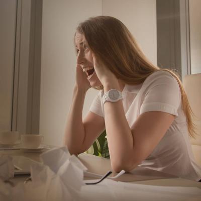 γυναίκα σε γραφείο εργασίας, απογοητευμένη και παρουσιάζοντας σημάδια burnout, με χαρτιά και άδεια φλιτζάνια καφέ γύρω της.