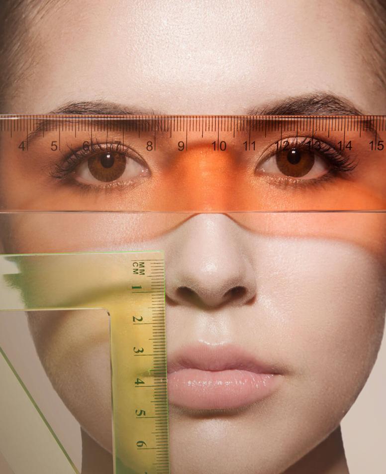 Κοντινό πλάνο γυναικείου προσώπου με διάφανους χάρακες τοποθετημένους πάνω του, επισημαίνοντας τη συμμετρία των χαρακτηριστικών. 